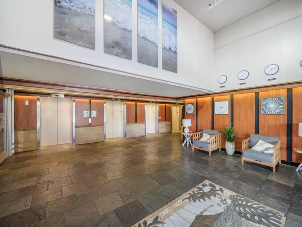 A spacious lobby with a high ceiling, wooden paneling, and a large open area with a patterned rug.