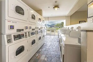A laundry facility with multiple washing machines and dryers, a tiled floor, and a view of the outdoors.