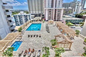 A rooftop pool area with multiple swimming pools, sun loungers, and wooden pergolas.