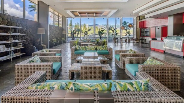 A spacious lobby with wicker furniture, a stone wall, and large windows offering a view of palm trees and buildings. - 23 FL-Cozy & Elegant King Studio (Honolulu)
