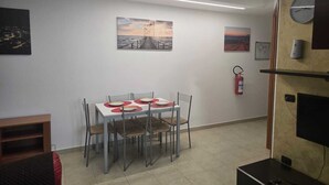 Un coin repas avec une table dressée pour quatre personnes, un extincteur fixé au mur et des œuvres d’art accrochées au-dessus de la table.