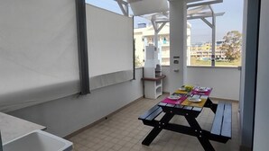 Un patio couvert avec une table de pique-nique aménagée pour les repas, un évier blanc et une vue sur les bâtiments en arrière-plan.