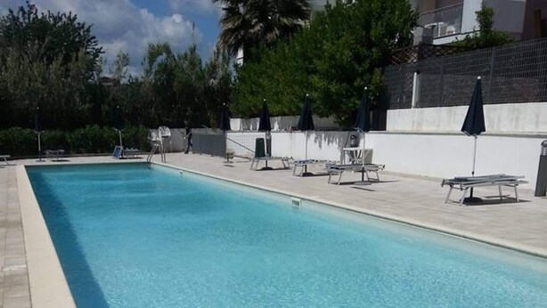Une piscine rectangulaire à l’eau d’un bleu limpide, entourée d’une terrasse carrelée et ombragée par des parasols.