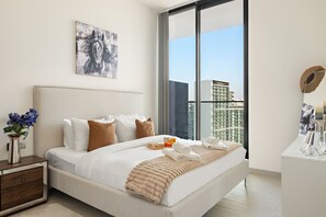 A modern hotel room with a large bed, a nightstand, a desk, and a view of the city through a large window. - Binghatti Onyx - 1413 1BD (Dubai)