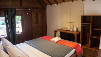 A room with a bed, a wooden wardrobe, a small table with a lamp, and a window with curtains.