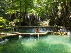 Una persona sentada en una piscina cristalina con una cascada al fondo.