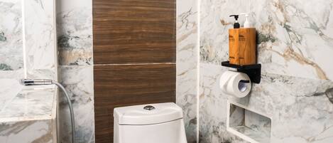 A bathroom with a toilet, a wooden shelf with toiletries, and marble walls.