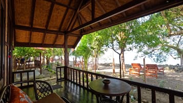 A covered outdoor seating area with a view of a landscaped garden and beach.
