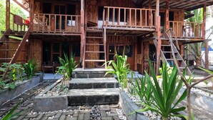 A wooden building with a balcony, steps, and a garden area with plants. - Maryan Moyo Bungalows and resto (Moyo)