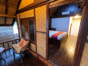 A room with a bed, a chair with cushions, a window with shutters, and a wooden ceiling. - Maryan Moyo Bungalows and resto (Moyo)