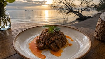A plate of food with a sauce, a glass jar with greenery, and a view of a sunset over water.