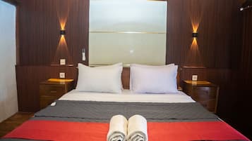 A hotel room with a large bed, two bedside tables, a nightstand, a wall-mounted light fixture, and a window.