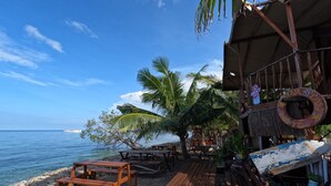 A beachside restaurant with wooden tables and benches, a thatched roof, and a view of the ocean. - Maryan Moyo Bungalows and resto (Moyo)