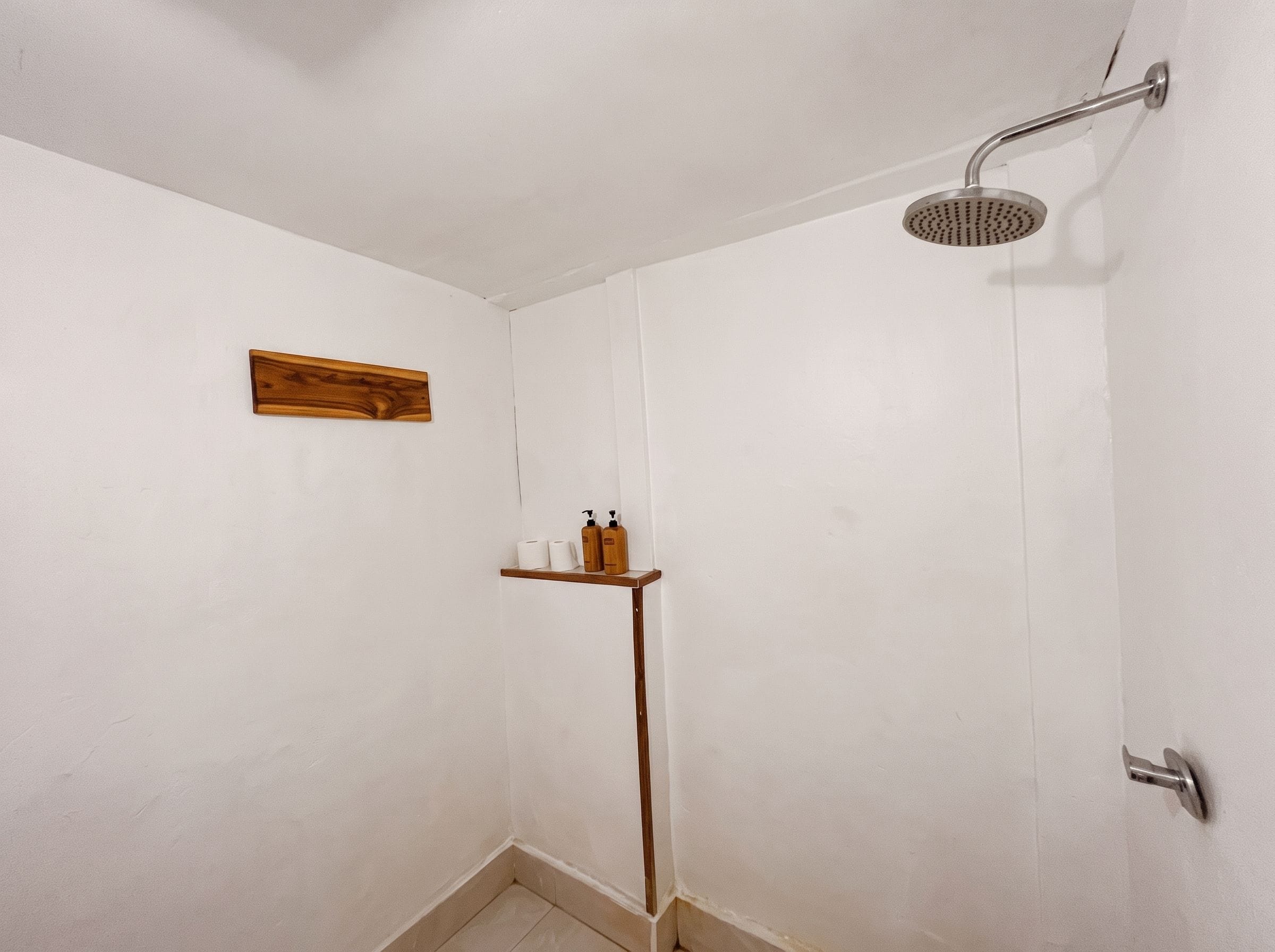 A shower with a handheld showerhead, a wooden shelf with toiletries, and a towel rack on the wall.