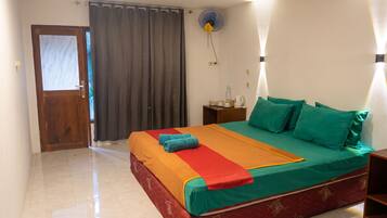 A hotel room with a bed, a nightstand, a fan, and a door.