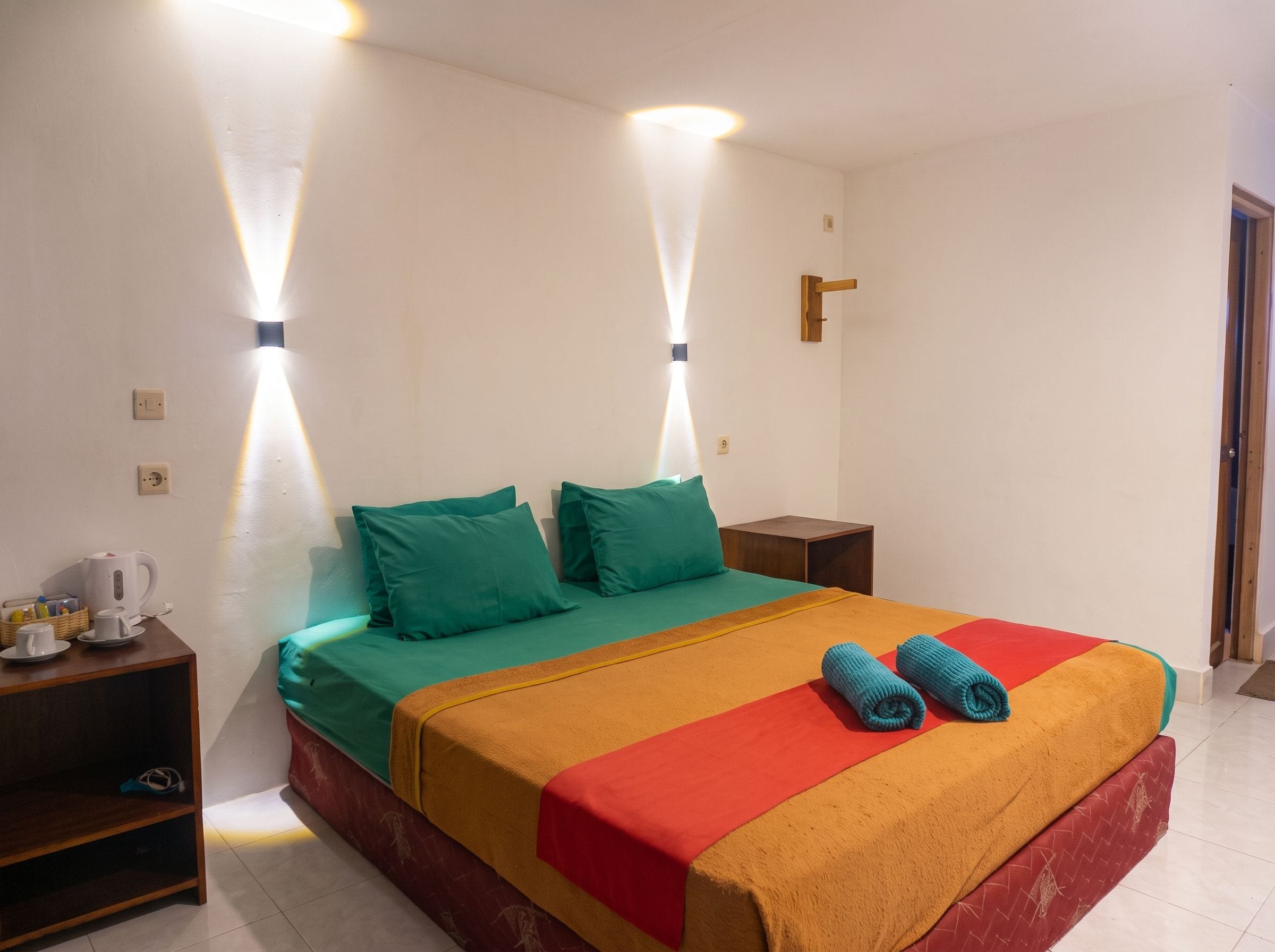 A hotel room with a bed, a bedside table, and a wall-mounted light fixture.