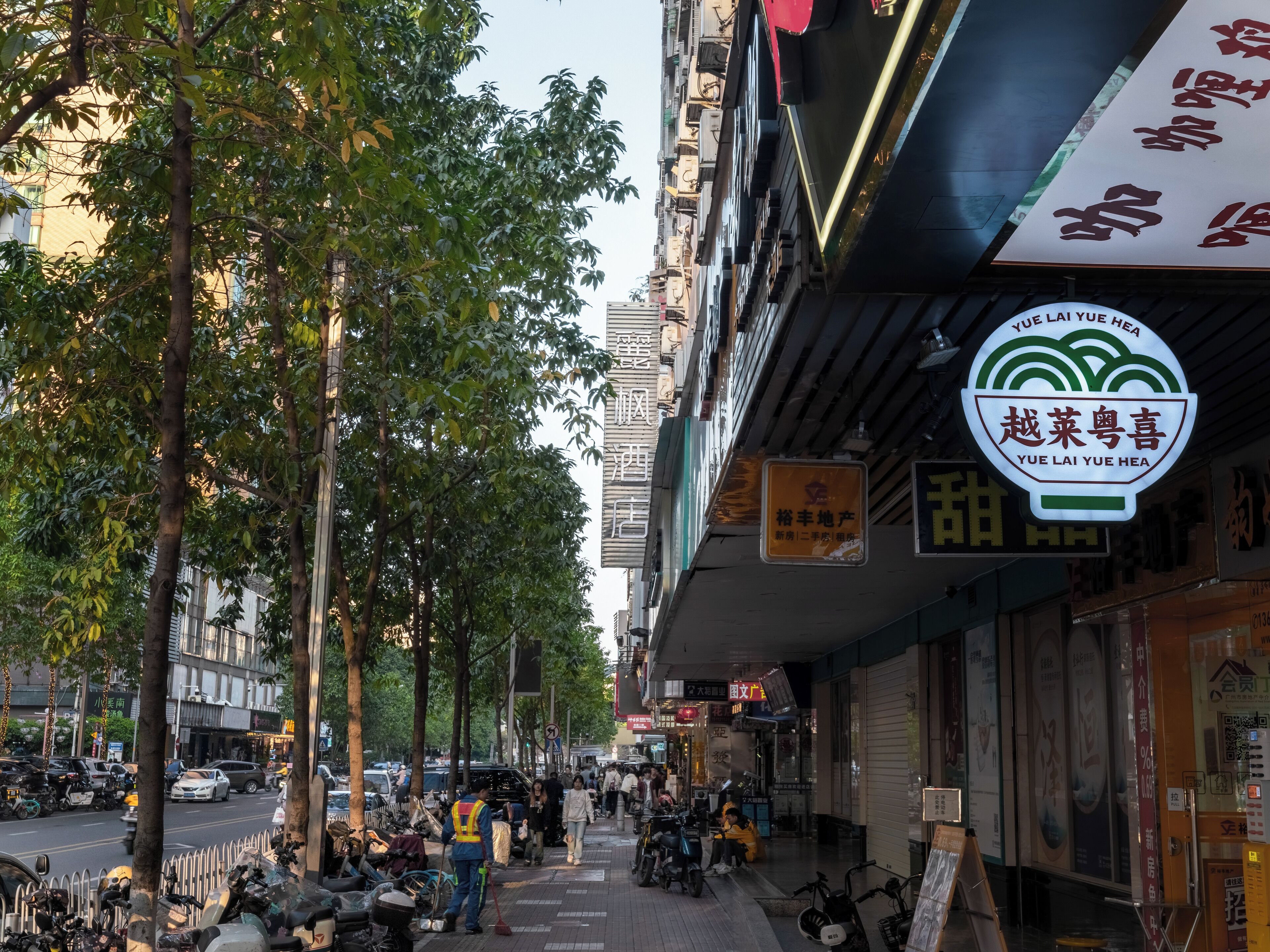 A street scene with a restaurant sign, parked scooters, and pedestrians.