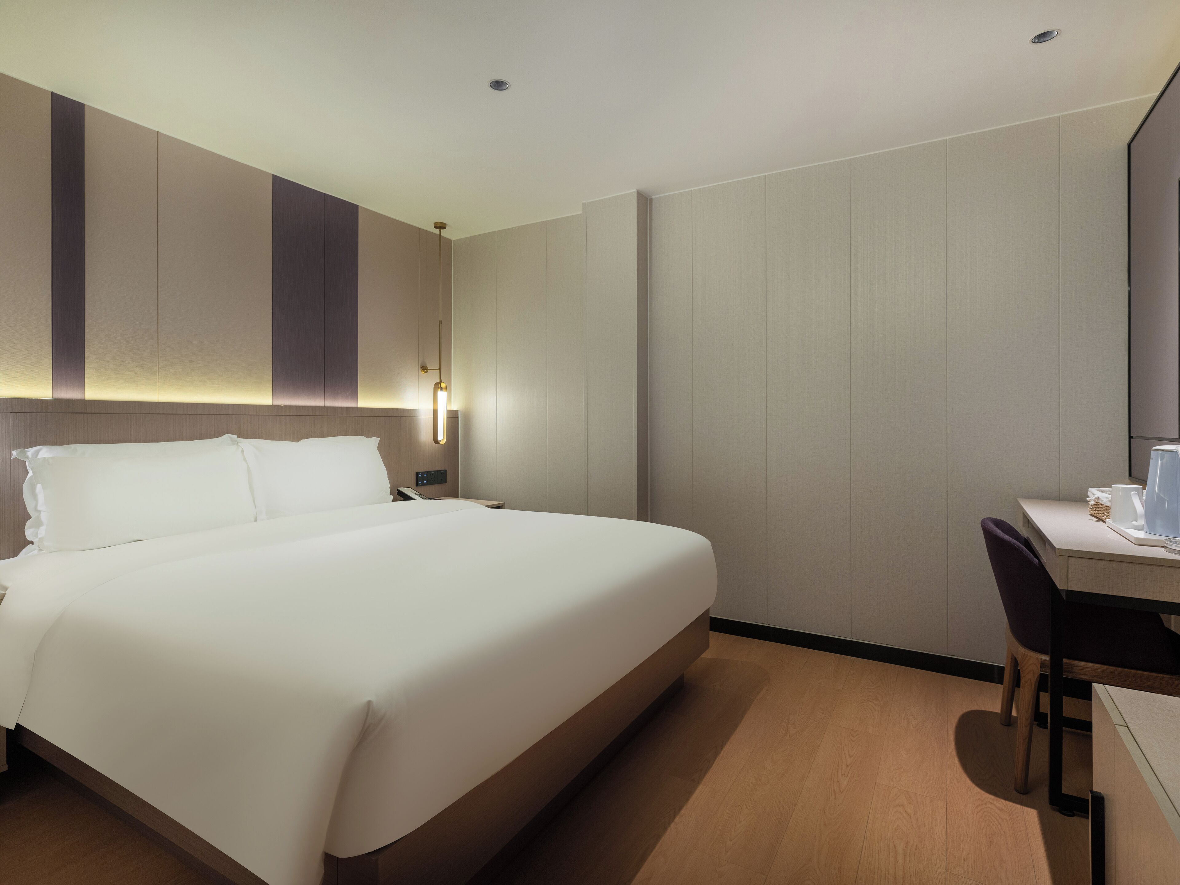 A hotel room with a large bed, a desk with a chair, and a nightstand with a lamp.