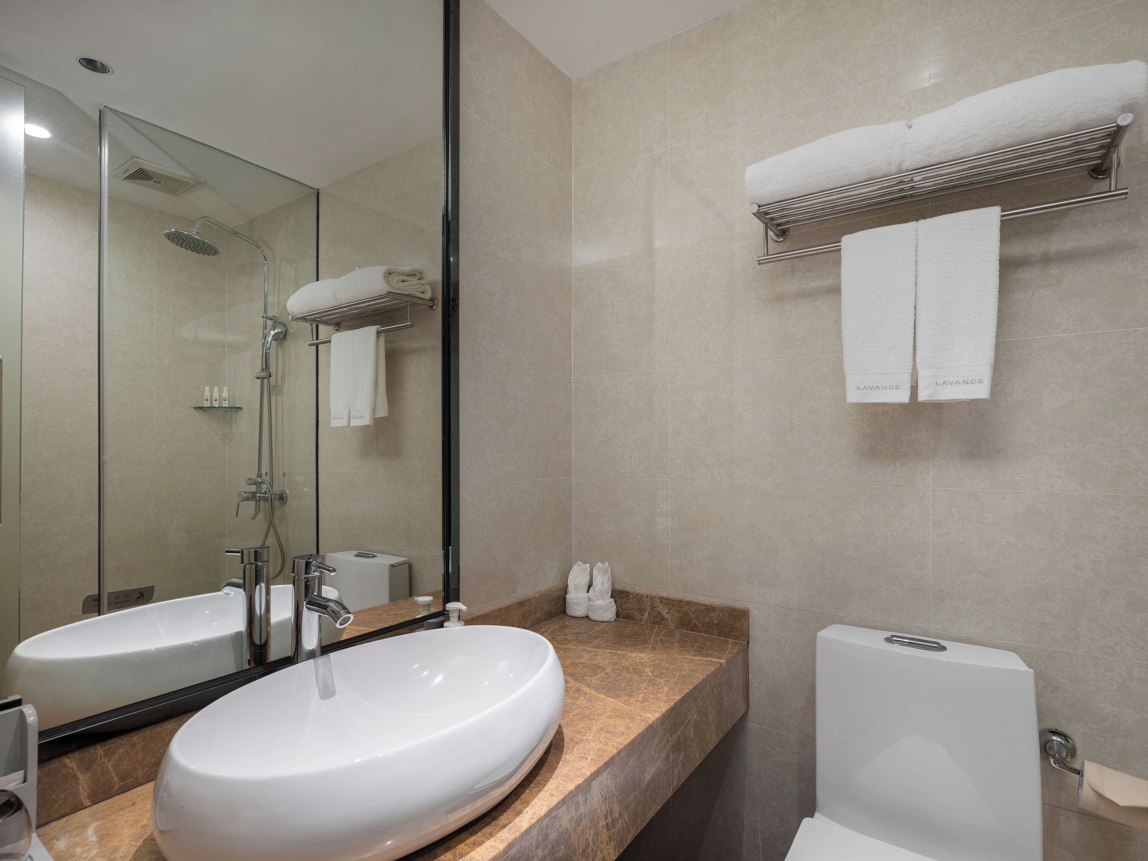 A modern bathroom with a large mirror, two sinks, a shower, and a toilet.
