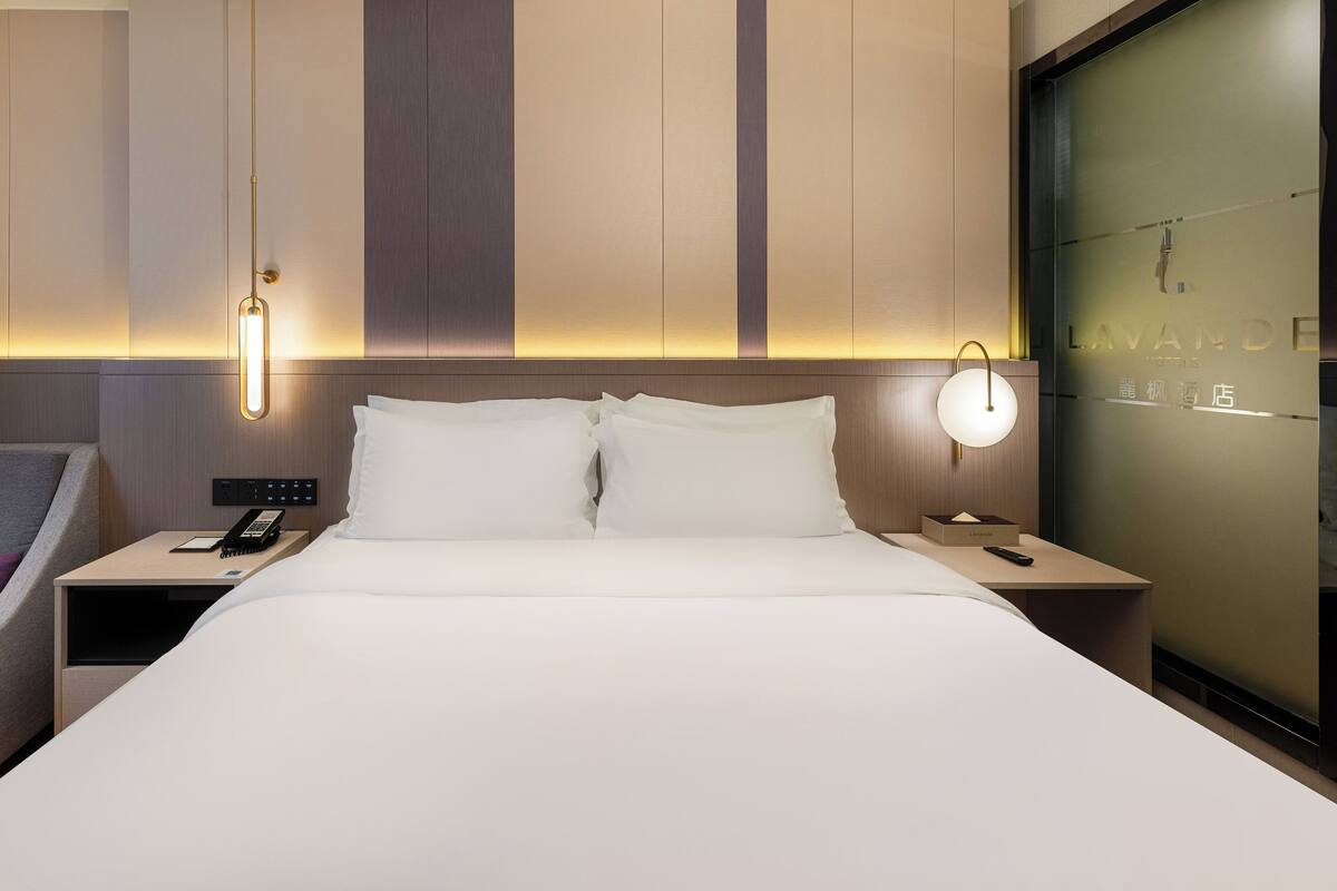 Habitación de hotel con una cama grande, mesitas de noche, un teléfono y una lámpara de pared.