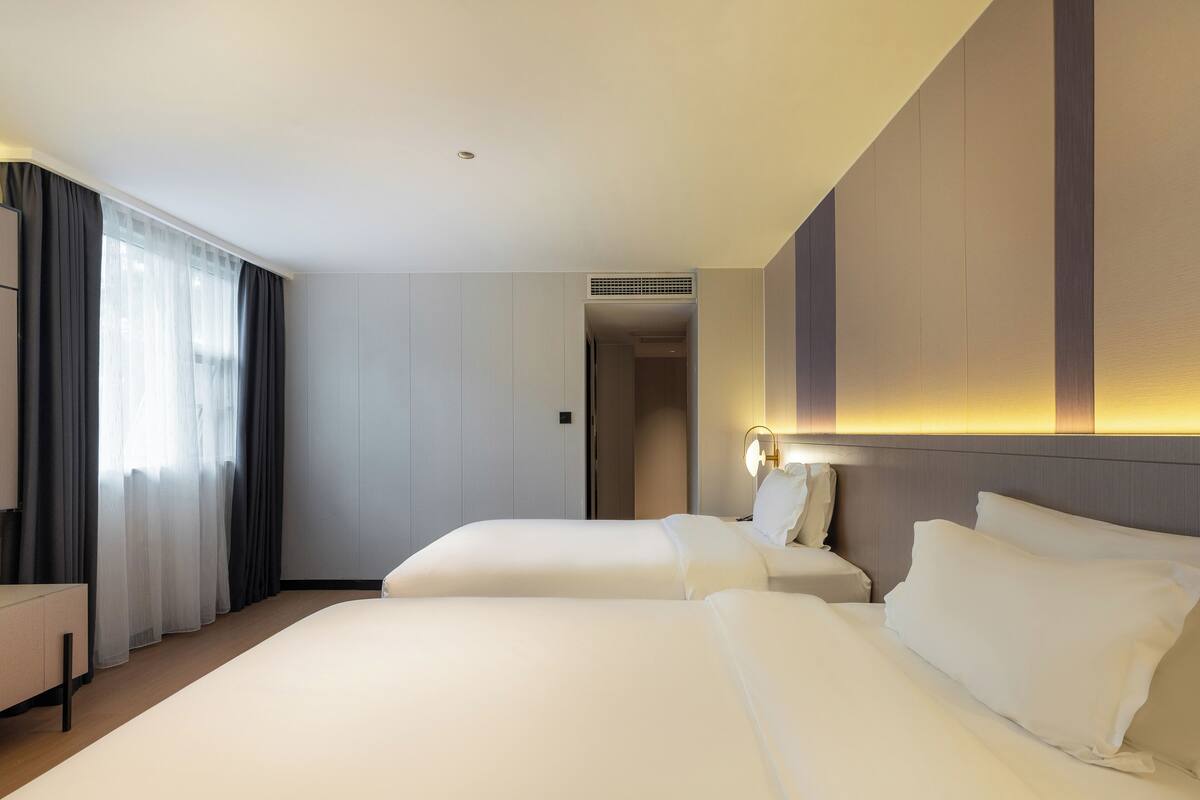 Una habitación de hotel con dos camas, un escritorio y un ventanal grande con cortinas.