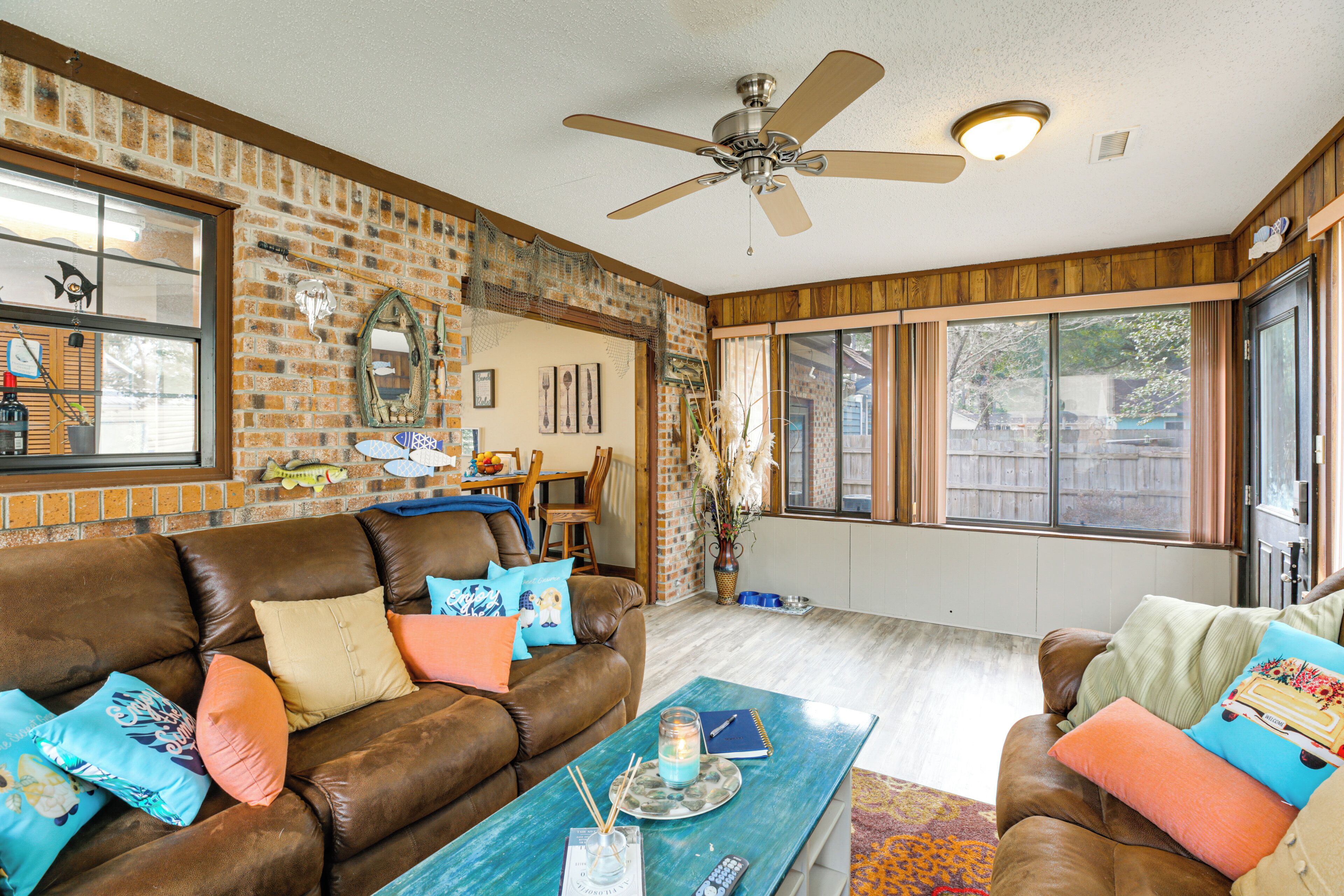 A spacious living room with a brown leather couch, a blue coffee table, and a ceiling fan.