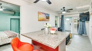 A kitchen with granite countertops, a dining area with orange chairs, and a ceiling fan. - Steps to Shore: Walkable Clearwater Beach Condo (Clearwater)