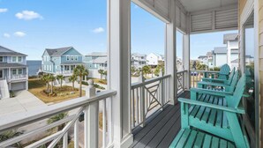 A porch with teal Adirondack chairs, a view of neighboring houses, and a clear sky.