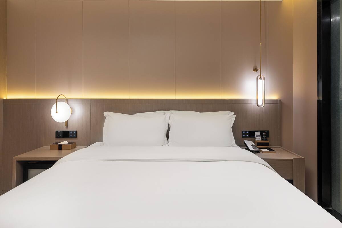 Une chambre d’hôtel moderne avec un grand lit, des tables de chevet, un panneau de commande et un luminaire suspendu.