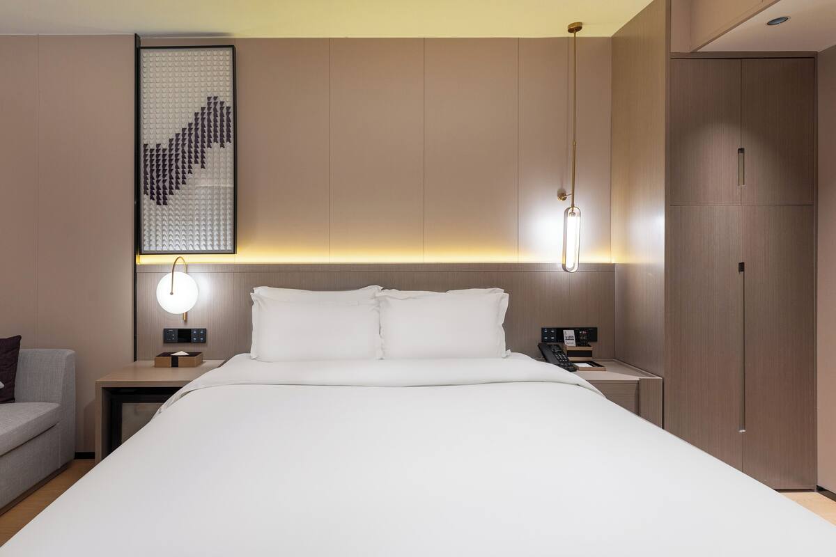 Une chambre d’hôtel moderne, dotée d’un grand lit, de tables de chevet, d’un bureau et d’une armoire.