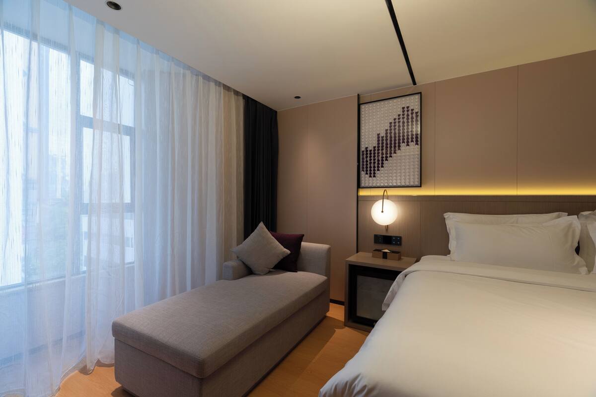 Une chambre d’hôtel moderne, dotée d’un grand lit, d’un canapé, d’une petite table et d’une œuvre d’art accrochée au mur.