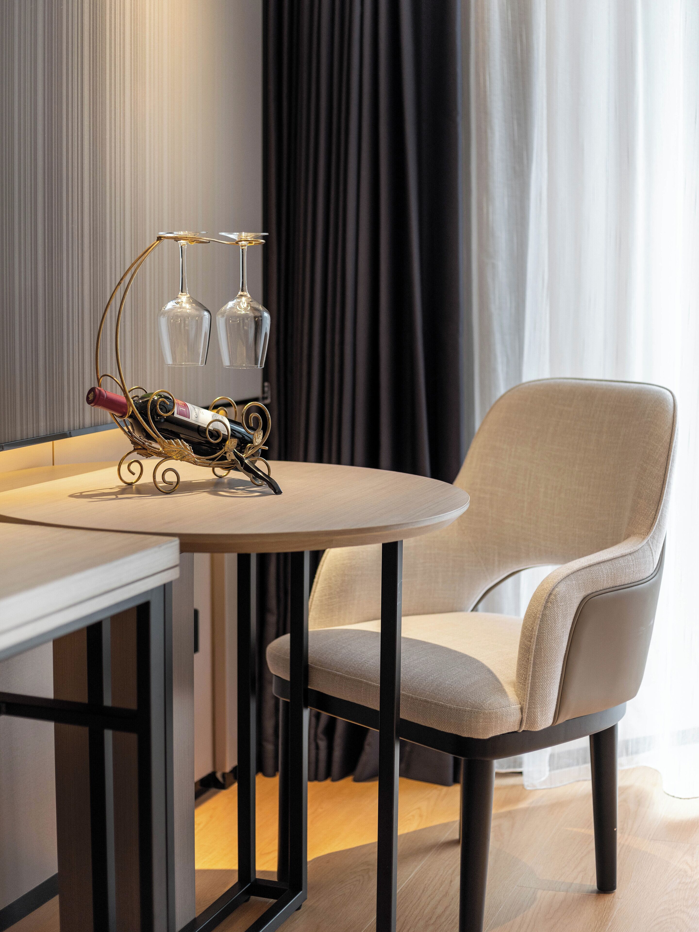 Una habitación moderna con una mesa redonda, una silla y una estantería decorativa para vinos y copas.