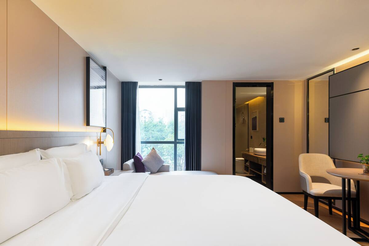 Une chambre d’hôtel avec un grand lit, un bureau, une chaise et une salle de bain visible à travers une porte ouverte.