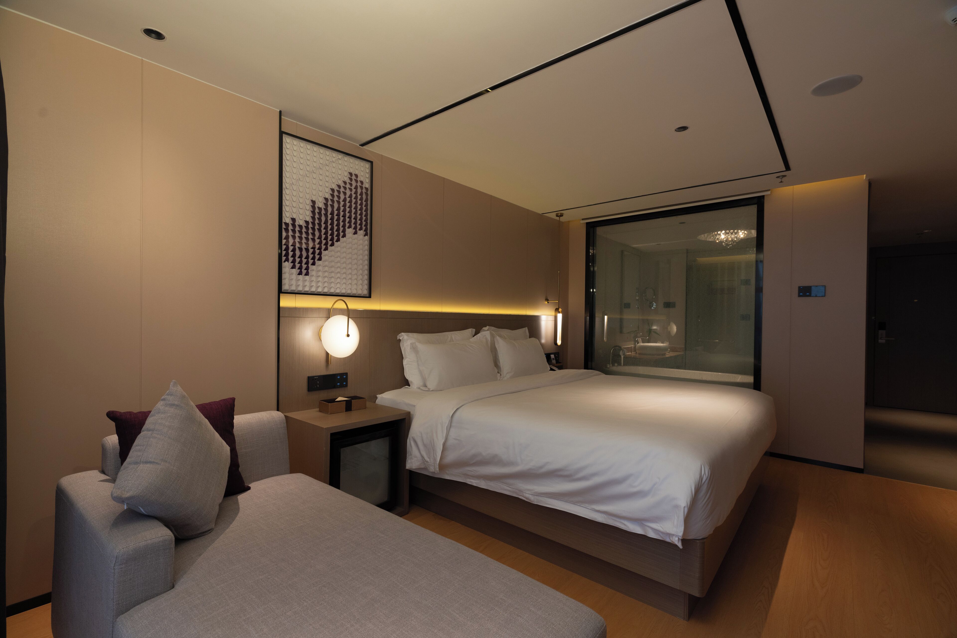 Ein modernes Hotelzimmer mit einem großen Bett, einem Nachttisch, einem Sessel und einem Glaskastenbad.