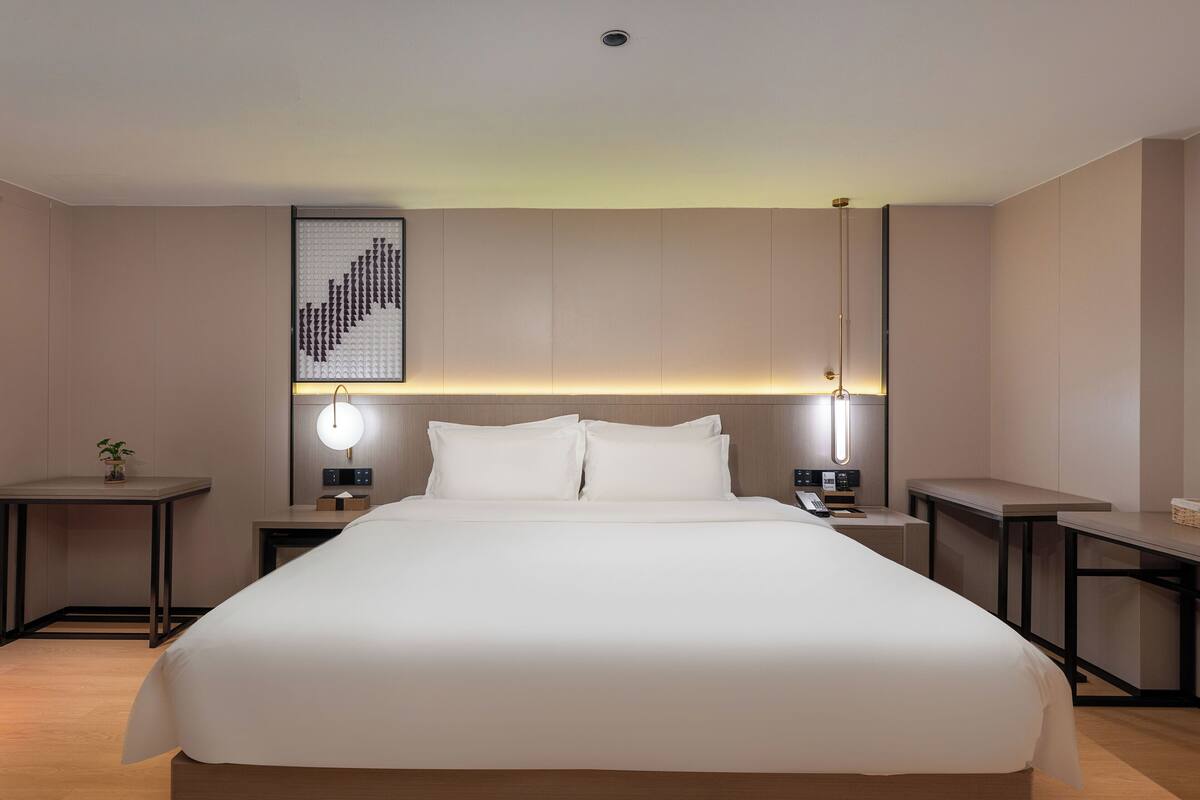 Une chambre d’hôtel moderne avec un grand lit, des tables de chevet, une œuvre d’art accrochée au mur et un luminaire fixé au plafond.