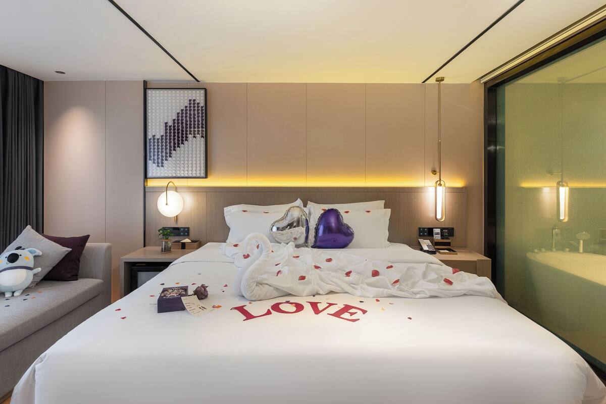 Une chambre d’hôtel moderne avec un lit bien fait, une table de chevet avec une lampe, une œuvre d’art accrochée au mur et une grande fenêtre.
