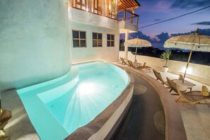 A swimming pool with lounge chairs and umbrellas, a wooden deck, and a view of the sky.