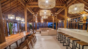 Un espace intérieur spacieux avec une longue table en bois, des sièges confortables et un coin bar avec des tabourets.
