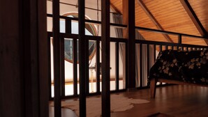 A room with a high ceiling, wooden beams, a bed with a floral bedspread, and a view through a window with a wooden frame. - Abant Cozy Homes (Bolu)