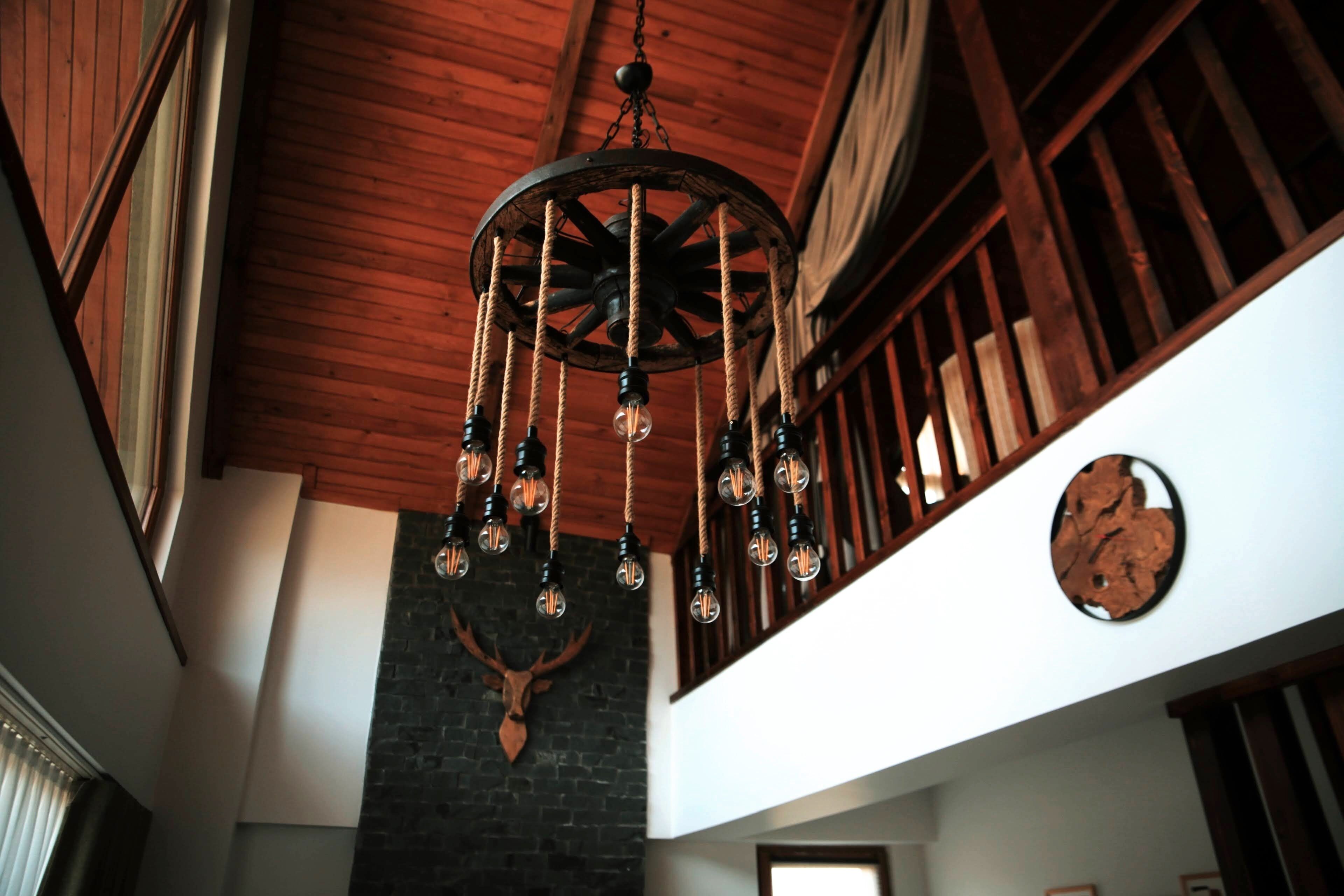 A room with a wooden ceiling, a stone wall with a deer head, and a hanging light fixture with multiple bulbs.
