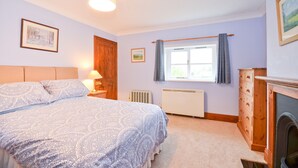 Une chambre avec un grand lit, une commode en bois, un radiateur et une fenêtre avec des rideaux.