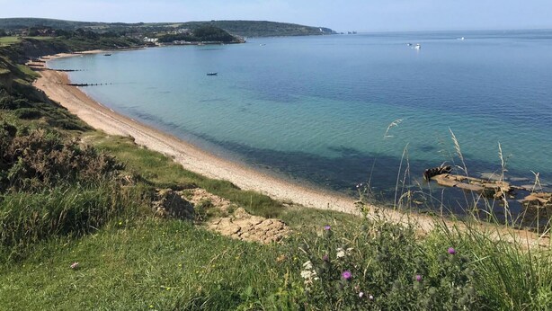 A coastal landscape with a sandy beach, clear blue water, and greenery. - Brambles Farm Bungalow (Freshwater)