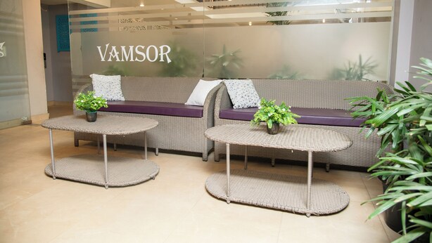 A reception area with a wicker sofa, two small tables, and potted plants. - 30 Vamsor Heights (Gurugram)