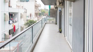 A balcony with a glass railing, potted plants, and air conditioning units. - 30 Vamsor Heights (Gurugram)