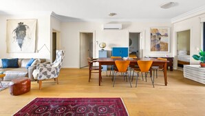 Un salon spacieux avec une table à manger en bois, un canapé et une table basse. On peut voir un globe terrestre sur une étagère et une plante sur le rebord de la fenêtre.