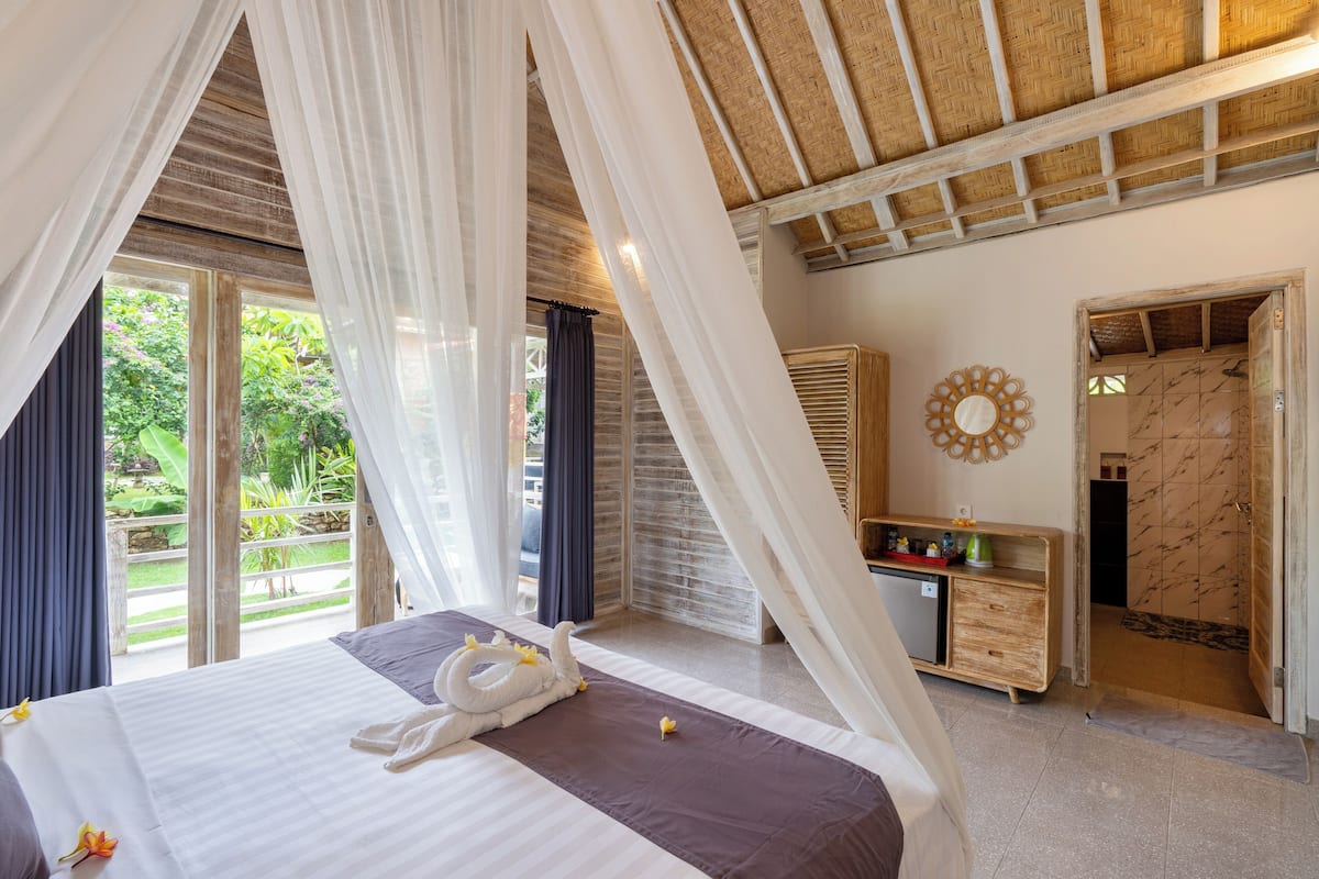 Une chambre à coucher avec un lit, une table de chevet, un miroir et une vue sur l’extérieur.