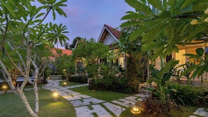 A well-maintained garden with a stone pathway leading to a building with a red roof. - Le Biu Garden View (Lembongan Island)