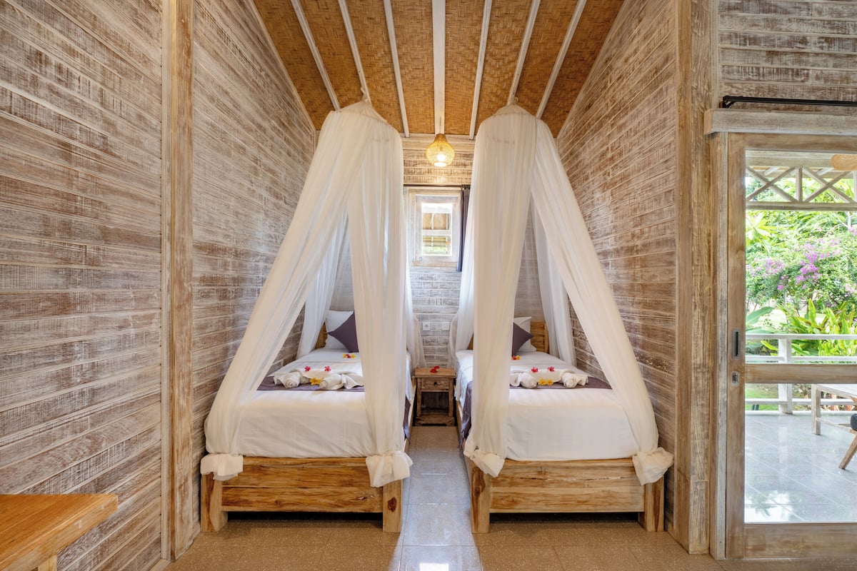 Une chambre avec deux lits en bois, chacun surmonté d’un baldaquin.