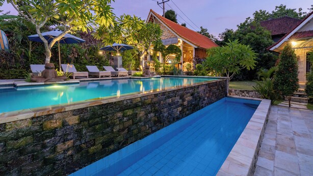 A swimming pool with lounge chairs and umbrellas, surrounded by stone walls and lush greenery. - Le Biu Garden View (Lembongan Island)