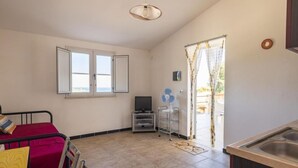 A small, well-lit room with a bed, a TV, a fan, and a window. - Residence Sole - Apartment 1 (Tertenia)